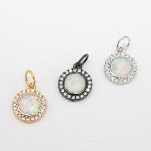 May include: Three pendant charms with a white opal stone surrounded by a halo of clear cubic zirconia stones. The charms are in gold, silver, and black.