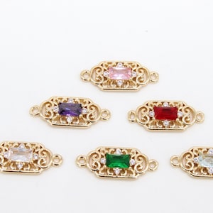 May include: Six gold-tone metal connector charms with different coloured gemstones. Each charm features a decorative filigree design and a rectangular gemstone in the centre. The gemstones are pink, purple, red, green, clear, and light blue.