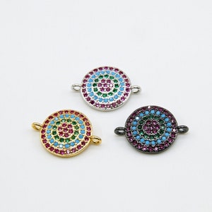 Puede incluir: Tres dijes redondos de metal decorativos con piedras redondas multicolores incrustadas. Los dijes son de oro, plata y negro.