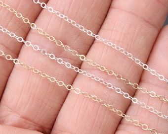 May include: Four different chain styles in silver and gold. The chains are laid out in a row on a hand.