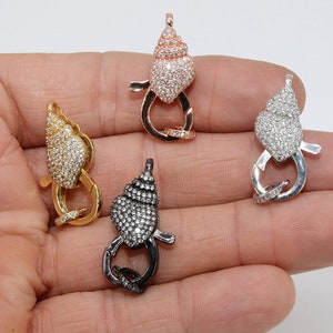 May include: Four different colored metal clasps in the shape of a seashell with clear rhinestones. The clasps are on a hand.
