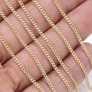 May include: A close-up of a gold chain necklace. The chain is made of small, linked circles and is laid out in a straight line on a hand.