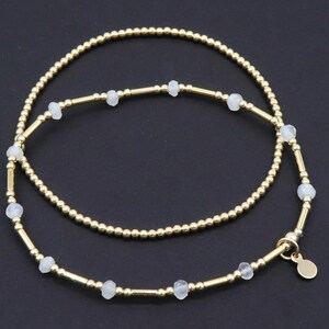 May include: Two gold-colored necklaces with small, round beads and interspersed with small, light-colored gemstones. One necklace is a simple strand of gold beads. The other necklace has a more intricate design with gemstones and gold bars.