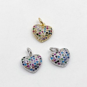 May include: Three heart-shaped charms with a pave setting of colorful gemstones. The charms are made of silver and gold metal.