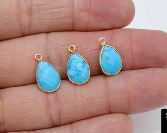 May include: Three turquoise teardrop-shaped pendants with gold-toned bezels and jump rings. The pendants are displayed on a hand.