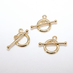 May include: Three gold-toned metal toggle clasps for jewelry making. Each clasp features a round ring and a straight bar that slides through the ring.