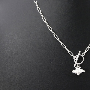 Op de afbeelding: Een zilveren ketting met een bij-bedel en een schuifgesp.