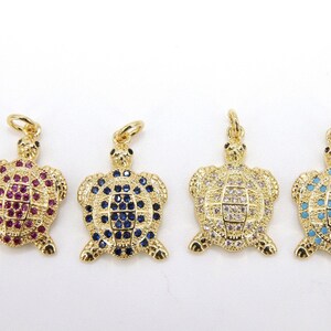 Op de afbeelding: Vier gouden schildpadbedels met verschillende gekleurde kristallen. De schildpadden zijn allemaal even groot en hebben dezelfde vorm, maar hebben verschillende gekleurde kristallen. De kristallen zijn rood, blauw, helder en turquoise.