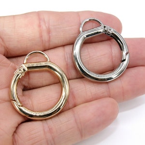 May include: Two metal key rings, one gold and one silver, with a spring-loaded clasp. The rings are shown in a hand.