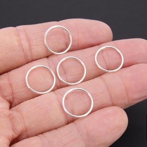 May include: Five silver jump rings, approximately 1.25 cm in diameter, are displayed on a hand.