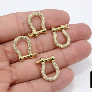 May include: Four gold-toned metal u-shaped clasps with clear crystal embellishments. Each clasp has a small bar across the top.