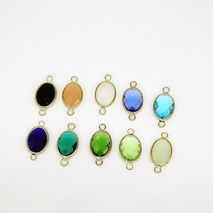 May include: Ten oval-shaped gemstone charms with gold-toned jump rings. The charms are in various colors, including black, peach, white, light blue, turquoise, dark blue, green, and light green.