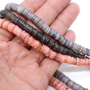 May include: A strand of multi-colored shell beads. The beads are in shades of pink, gray, and brown. The beads are round and flat, and they are strung on a clear thread.