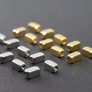 Może przedstawiać: Zbiór złotych i srebrnych metalowych zakończeń do sznurków lub pasków. Zakończenia są prostokątne z otworem w środku.