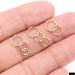May include: Several small, gold-colored rings are interlocked in various configurations, resting on a light-toned surface. The rings appear to be jewelry components, possibly for earrings or necklaces. The image is well-lit, highlighting the metallic sheen of the rings.