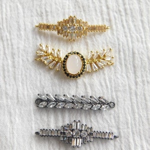 Puede incluir: Cuatro conectores de joyería diferentes de cristal y metal. El conector superior es de oro con cristales transparentes. El segundo conector es de oro con cristales transparentes y una piedra ovalada blanca. El tercer conector es de plata con cristales transparentes. El conector inferior es de plata con cristales transparentes en forma de cruz.