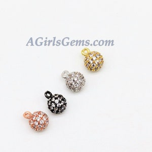 May include: Four small, round, ball-shaped charms with a loop at the top. Each charm is covered in clear rhinestones and is available in gold, silver, black, and rose gold.