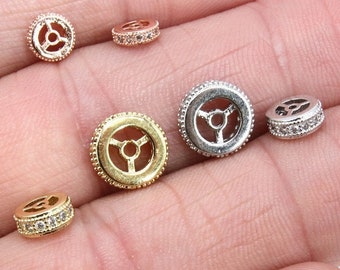 May include: A collection of six gold and silver round bead spacers with a decorative design. The spacers are set with clear cubic zirconia stones.