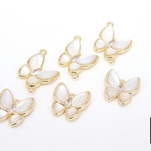 May include: Six gold butterfly charms with white mother of pearl wings and clear rhinestone accents. The charms have a loop on the top for attaching to jewelry.