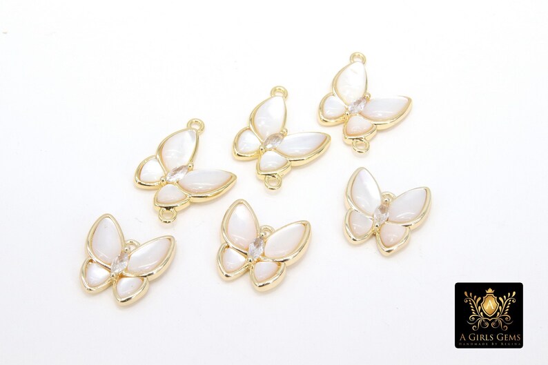 May include: Six gold butterfly charms with white mother of pearl wings and clear rhinestone accents. The charms have a loop on the top for attaching to jewelry.