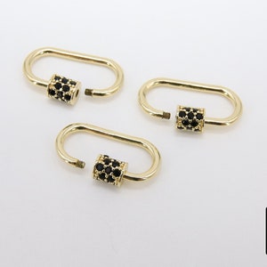 May include: Three gold-colored oval screw lock clasps with black gem accents. The clasps are open, revealing the screw threads. The background is plain white. The clasps are likely for jewelry making.
