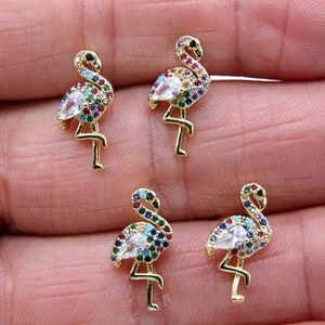 May include: Four gold-tone flamingo earrings with colorful crystal accents. Each earring features a white crystal in the center of the flamingo's body.
