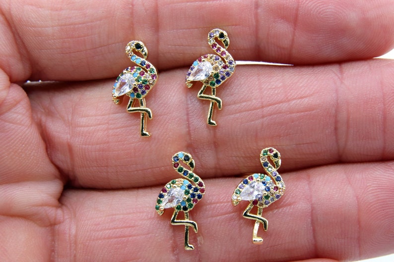 May include: Four gold-tone flamingo earrings with colorful crystal accents. Each earring features a white crystal in the center of the flamingo's body.