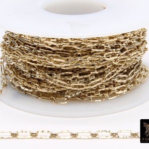 May include: A spool of gold-colored chain, wound around a white plastic spool. The chain is a delicate, flat, oval link chain.