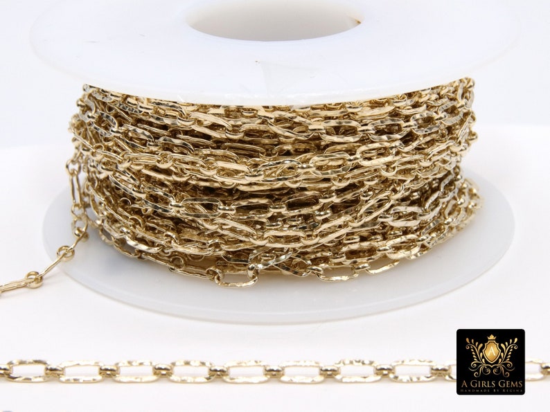 May include: A spool of gold-colored chain, wound around a white plastic spool. The chain is a delicate, flat, oval link chain.