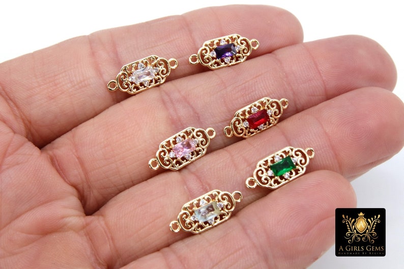 May include: Six gold-tone connector charms with ornate filigree designs and a variety of coloured gemstones in the centre. The gemstones are purple, red, pink, green, and light blue.