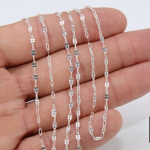May include: A silver chain necklace with a delicate, patterned design. The chain is made of small, oval-shaped links that are connected together to create a continuous loop.
