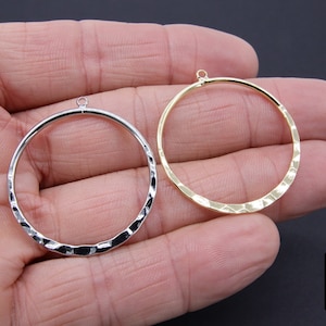 May include: Two hammered metal hoops with a jump ring at the top. The hoop on the left is silver and the hoop on the right is gold.