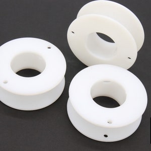 May include: Three white plastic spools with a center hole. The spools are stacked on top of each other.