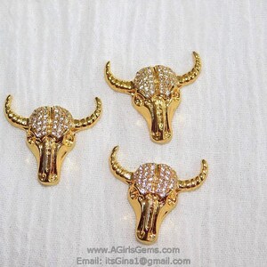 May include: Three gold-tone bull head charms with clear rhinestone accents. The charms are approximately 1 inch in size.
