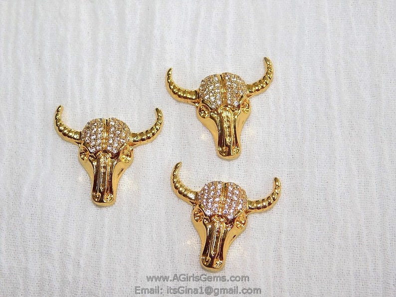 May include: Three gold-tone bull head charms with clear rhinestone accents. The charms are approximately 1 inch in size.