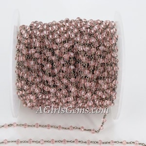 May include: A spool of pink glass beads and silver chain, ideal for making jewellery or rosaries. The chain is wound around the spool and the beads are visible. The text "AGirlsGems.com" is printed on the spool.
