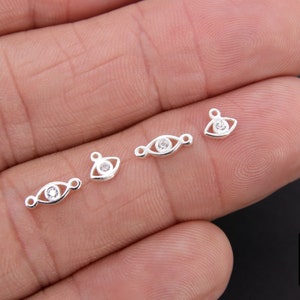 May include: Four silver eye charm pendants with clear rhinestones. The charms are on a hand.