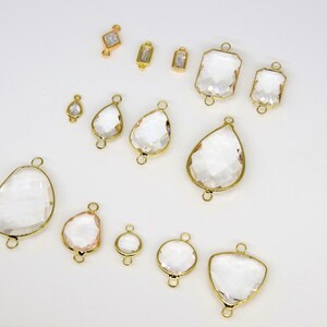 May include: Assortment of clear glass crystal charms with gold-toned metal accents. The charms are in various shapes, including teardrop, oval, square, and rectangular.