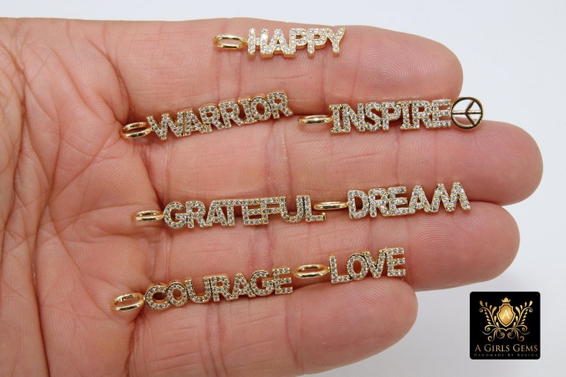 May include: A set of gold charm necklaces with various words set in diamonds, including "Happy", "Warrior", "Inspire", "Grateful", "Dream", "Courage", and "Love".