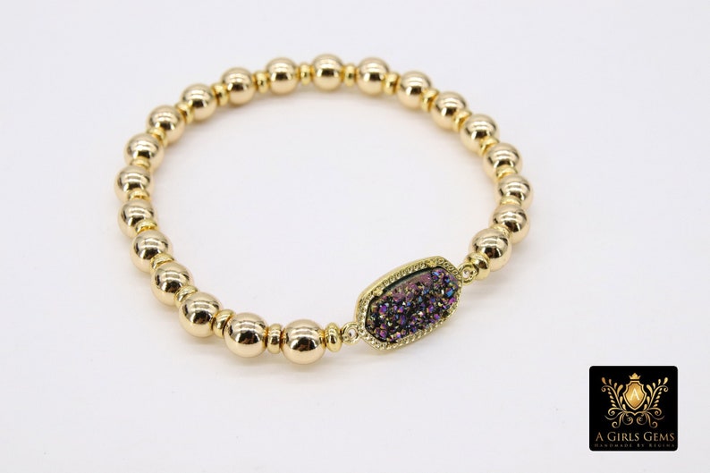 May include: Gold beaded bracelet with a purple and iridescent gemstone charm. The charm is oval shaped and has a gold setting.