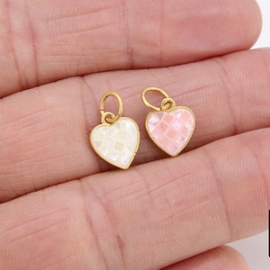 May include: Two gold heart-shaped charms with a textured surface. One charm is white and the other is pink.