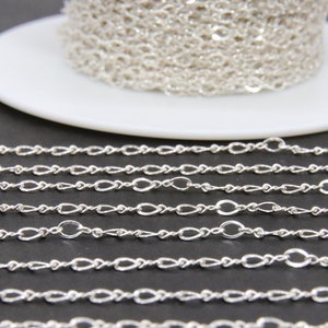 May include: A silver chain with a twisted oval link design. The chain is coiled on a white spool and laid out in rows on a black surface.
