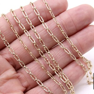 May include: A close-up of a gold chain necklace with a delicate, textured design. The chain is made of multiple strands and is lying on a hand.