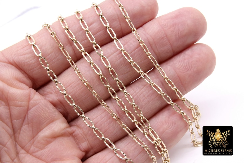 May include: A close-up of a gold chain necklace with a delicate, textured design. The chain is made of multiple strands and is lying on a hand.