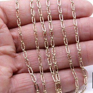 May include: A close-up of a gold chain necklace with a textured, oval-shaped link. The chain is laid out on a hand, showing the detail of the links.