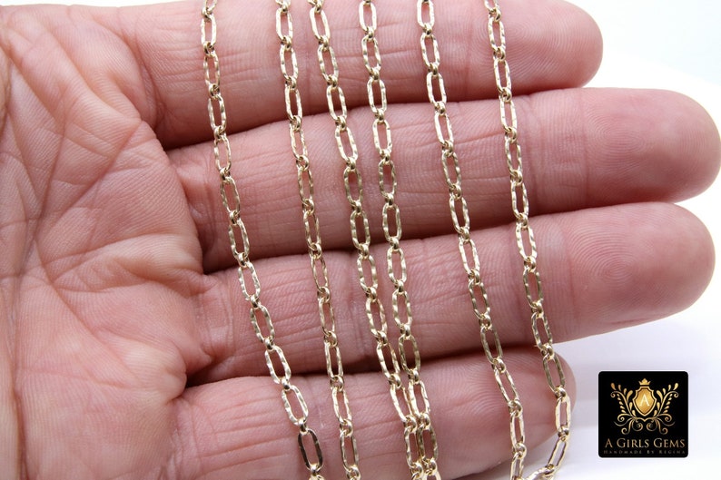 May include: A close-up of a gold chain necklace with a textured, oval-shaped link. The chain is laid out on a hand, showing the detail of the links.