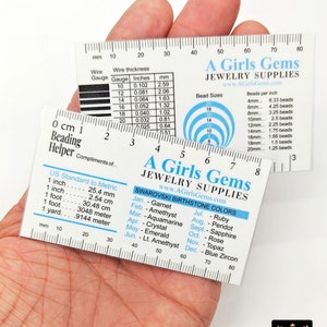 May include: A clear plastic ruler with a white background and black markings. The ruler has a measurement scale in both inches and millimetres. The ruler also includes a chart for wire gauge and thickness, a chart for bead sizes and beads per inch, and a chart for Swarovski birthstone colours.