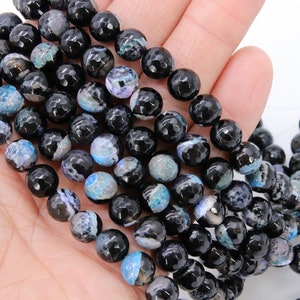 May include: Strands of black faceted gemstone beads with blue and gray accents. The beads are round and have a textured surface. The beads are likely used for jewelry making.