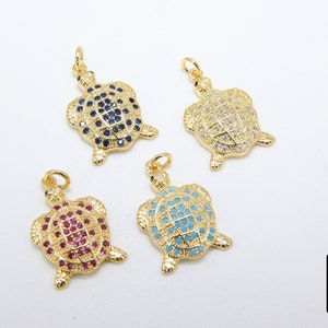 Op de afbeelding: Vier gouden schildpadbedels met verschillende kristalaccenten. De schildpadden zijn versierd met blauwe, witte, roze en turquoise kristallen.