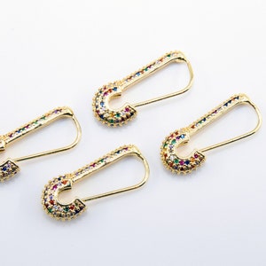 May include: Four gold safety pin earrings with colorful rhinestones. The earrings are on a white background.